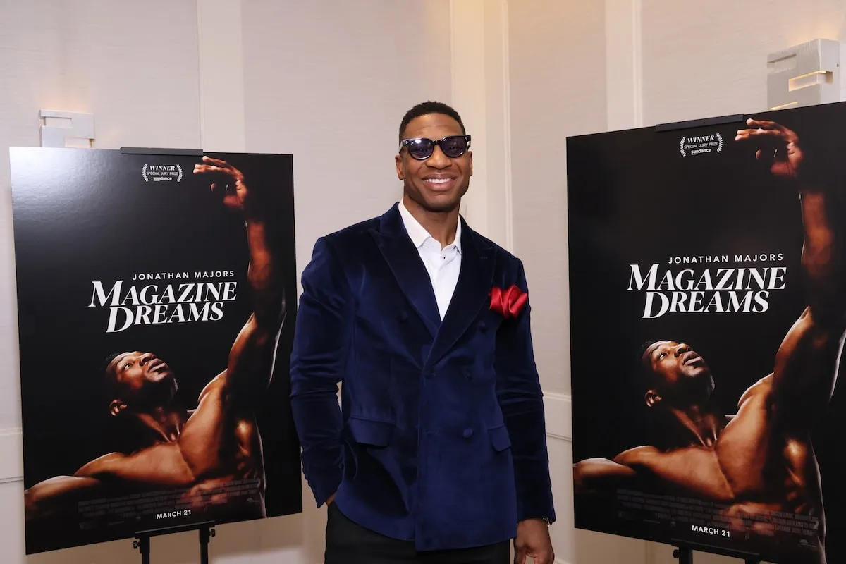 Portant une veste en velours bleu et un pantalon noir, Jonathan Majors sourit à une projection spéciale de 